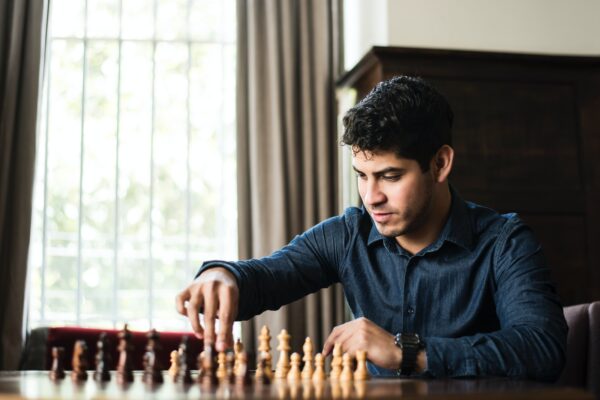 man in blue dress shirt sitting down and playing chess game