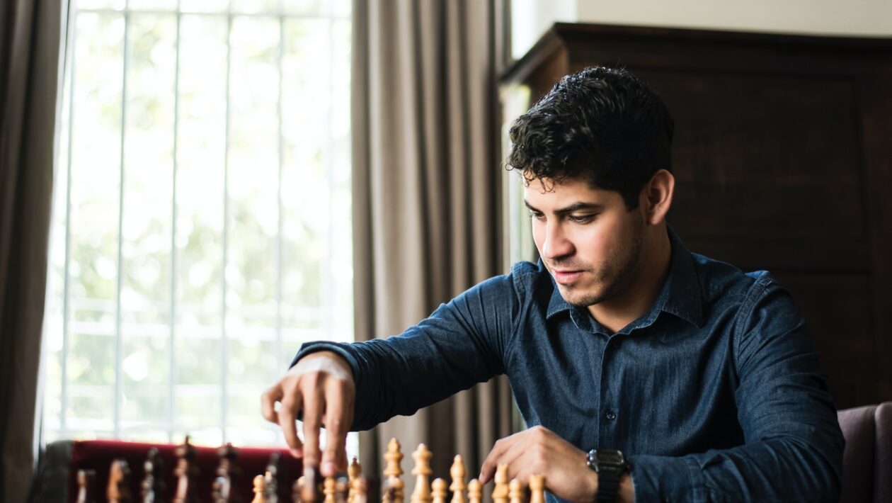 man in blue dress shirt sitting down and playing chess game